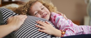 Young girl holding mothers baby bump in bed