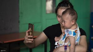 A woman takes a selfie with a baby on a street in Beijing on June 14, 2017. / AFP PHOTO / Nicolas ASFOURI        (Photo credit should read NICOLAS ASFOURI/AFP/Getty Images)